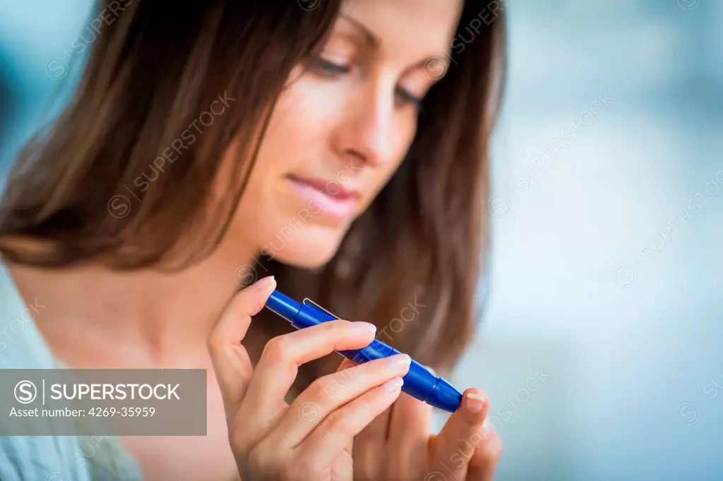 A diabetic person is checking her blood sugar level (self glycemia) A drop of blood obtained with a pen-like lancing device is placed on a test stick and analysed with blood glucose tester (glucometer)