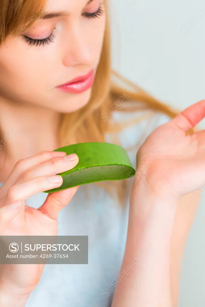 Woman applying an aloe vera leaf on the skin.