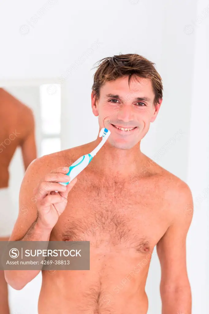 Man brushing her teeth with electric toothbrush.