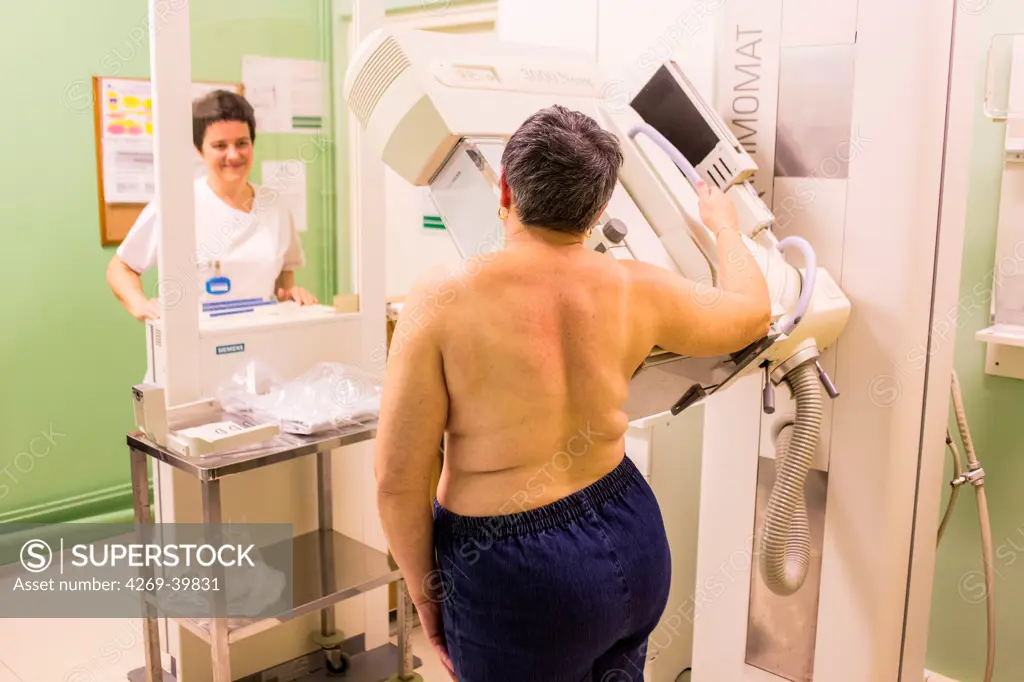 Radiographer positioning a woman's breast in an X-ray machine prior to taking a mammogram (breast X-ray), Angoulême hospital, France .