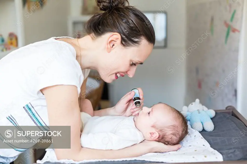Mother giving drops of vitamin D to a 3 month old baby boy.