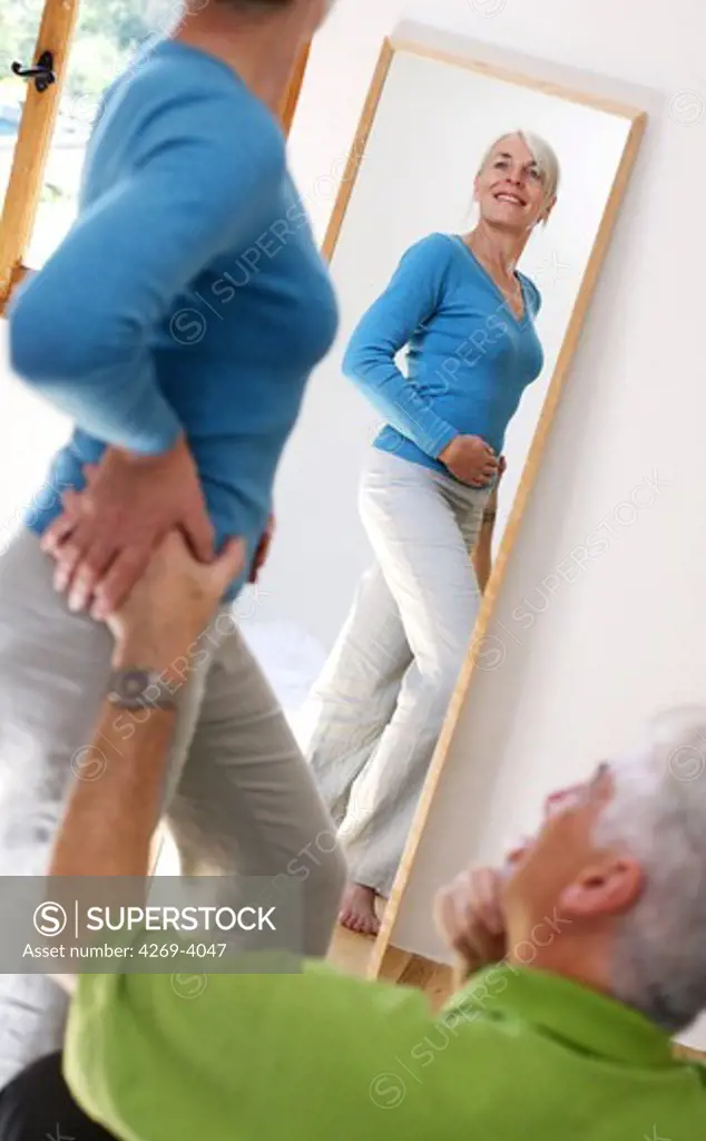 Senior woman looking at her body in a mirror.