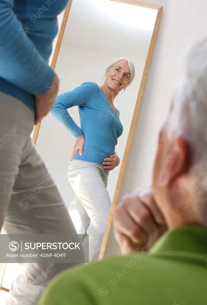 Senior woman looking at her body in a mirror.