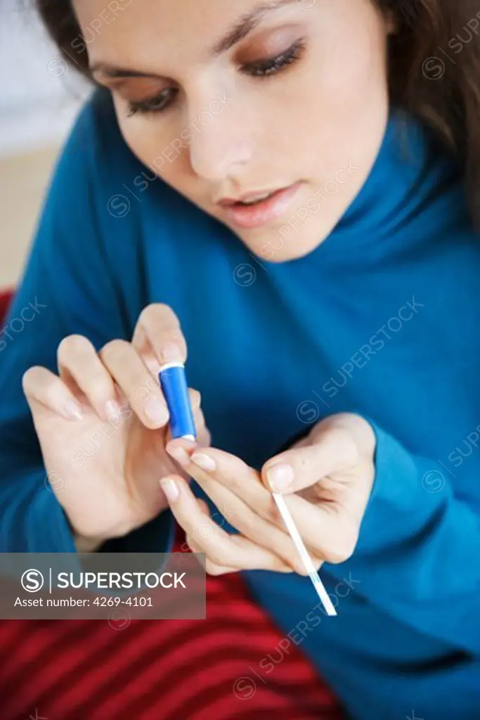 A diabetic person is checking her blood sugar level (self glycemia). A drop of blood obtained with a pen-like lancing device is placed on a test stick and analysed with blood glucose tester (glucometer).
