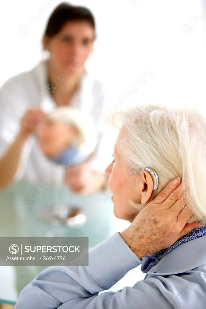 Hearing aid specialist fitting digital hearing aid to elderly woman.