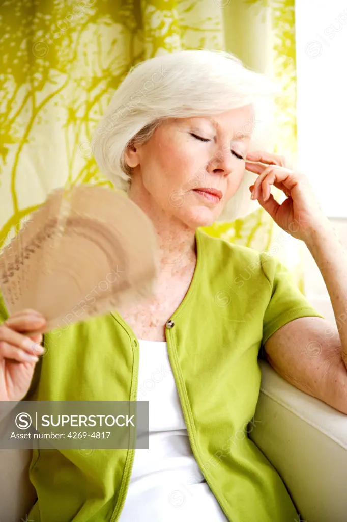Senior woman cooling her face with a fan.