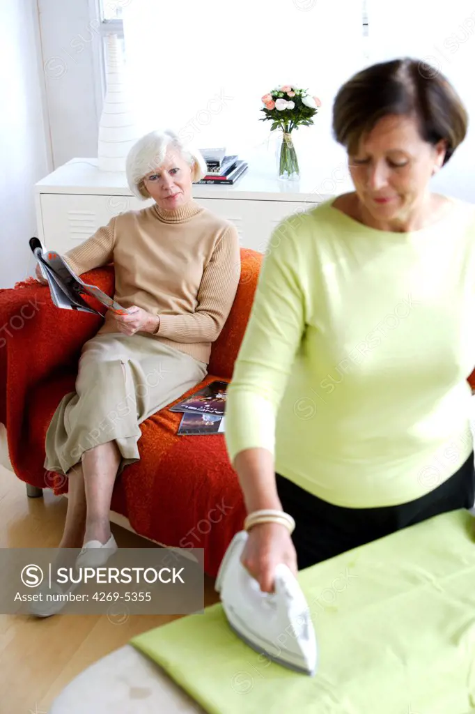 Woman ironing for of elderly woman at home.