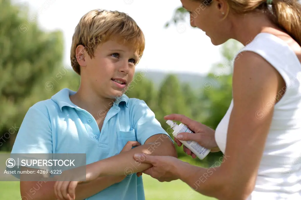 Woman applying spray on itchy skin of her son following insect bite.