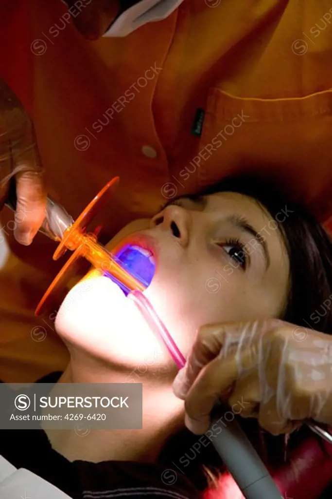 13 years old child receiving dental care. The dentist uses ultraviolet light to polymerize a photosensitive filling.