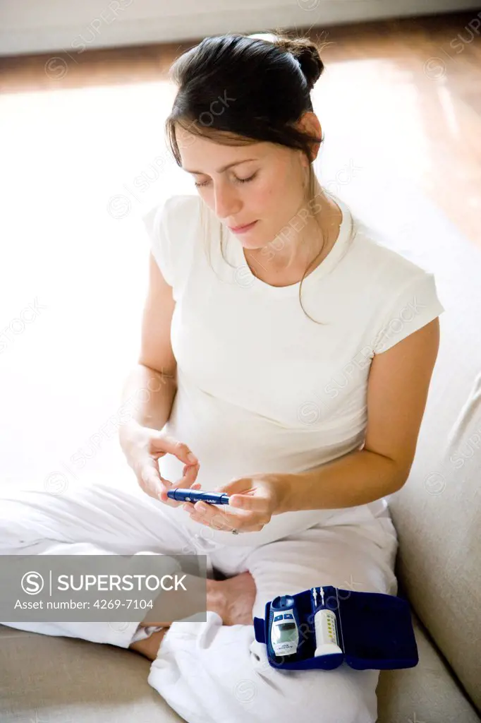 A diabetic pregnant woman is checking her blood sugar level (self glycemia). A drop of blood obtained with a pen-like lancing device is placed on a test stick and analysed with blood glucose tester (glucometer).