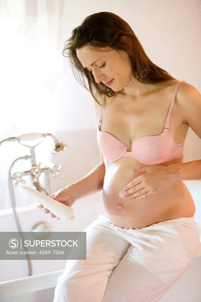 Pregnant woman applying cream against stretch marks.