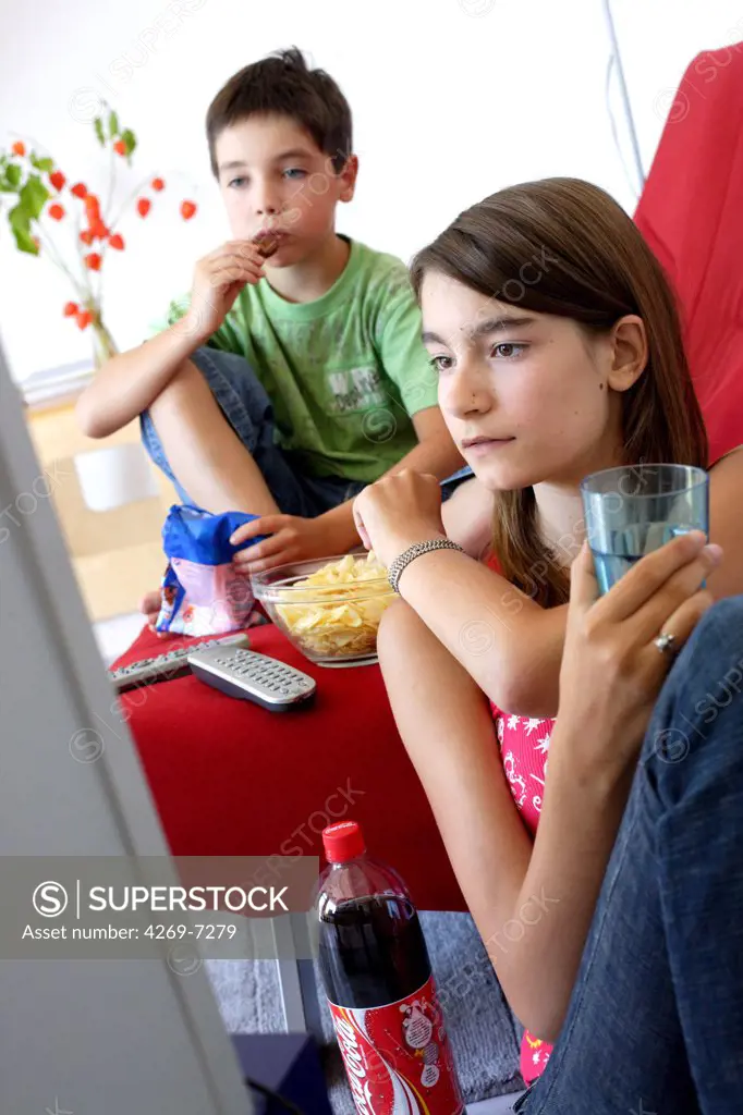 Child and teenage girl snacking while watching TV.