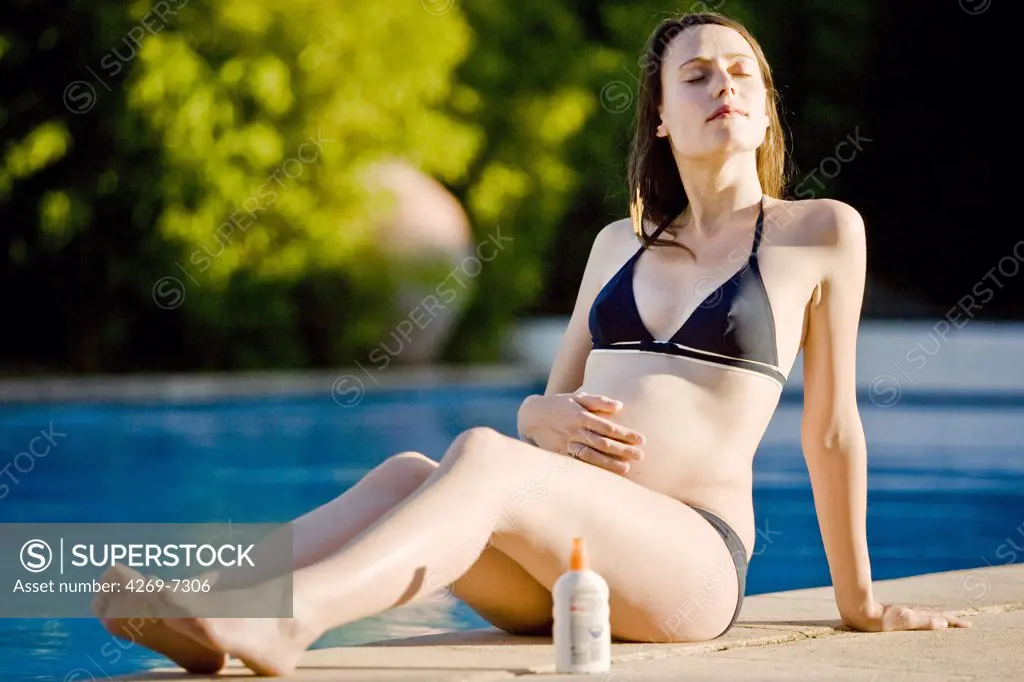 Pregnant woman sunbathing by a swimming pool.