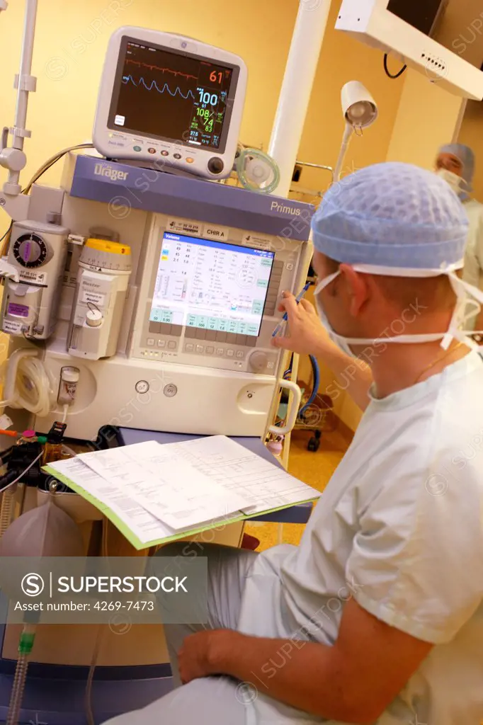 Anaesthetist beside anaesthetic monitoring equipment during surgery. The equipment supplies anaesthetic products that maintain the unconsciousness of the patient. The vital signs (heartbeat and breathing) are displayed on a monitor. Department of gastroenterological surgery, Limoges hospital, France.
