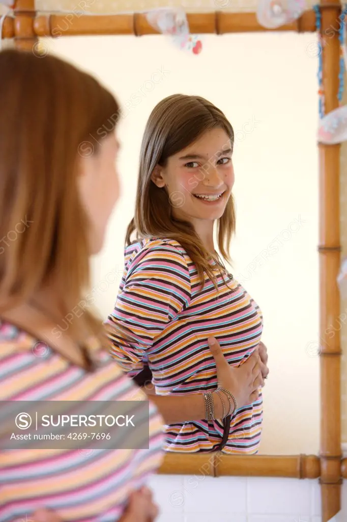 Teenage girl watching her breasts in a mirror.