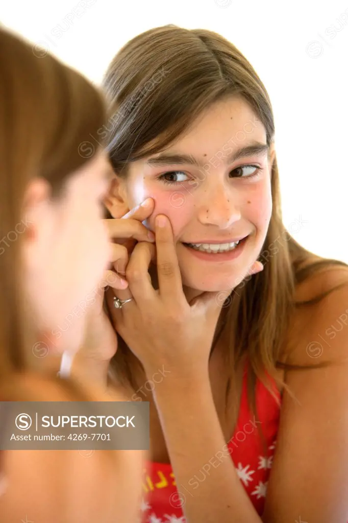 Teenage girl checking her face in the mirror, for acnea pimples or other skin problems.