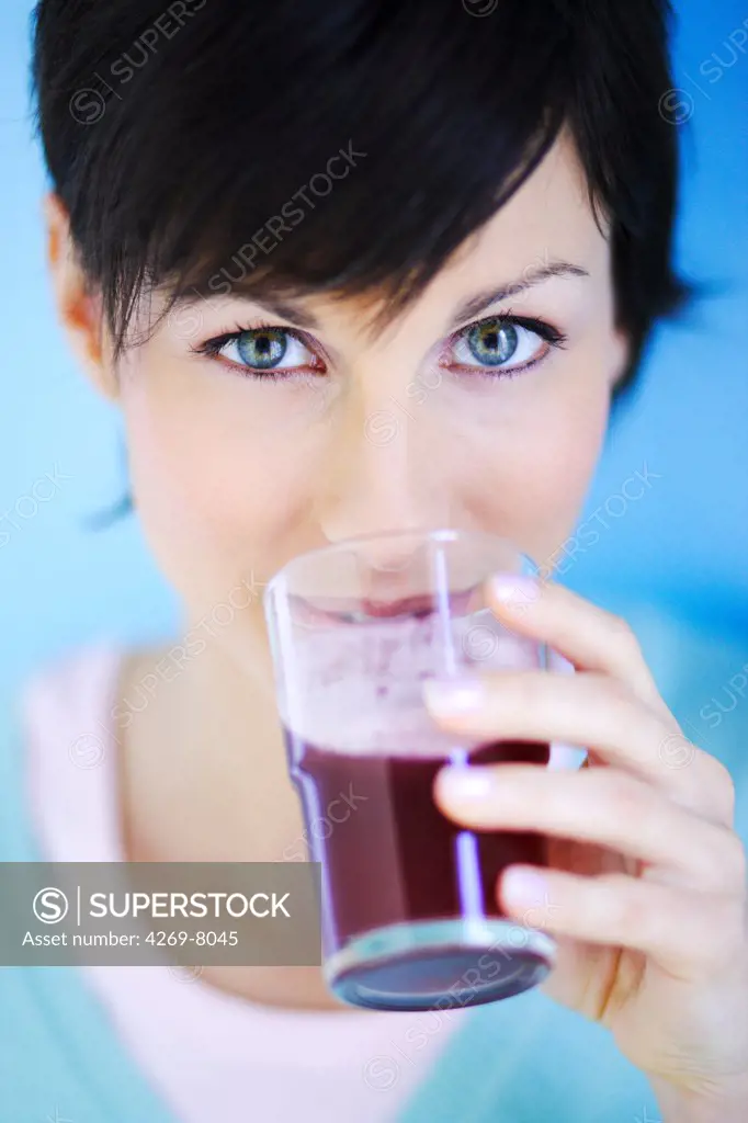 Woman drinking a glass of cranberry juice for cystitis prevention.