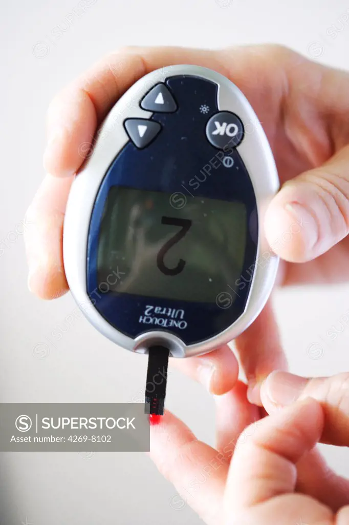 A diabetic person is checking her blood sugar level (self glycemia). A drop of blood obtained with a pen-like lancing device is placed on a test stick and analysed with blood glucose tester (glucometer).