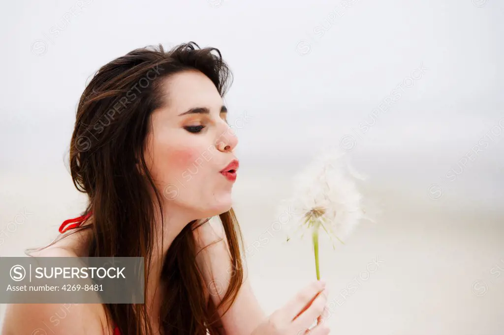 Woman blowing on a dandelion flower.
