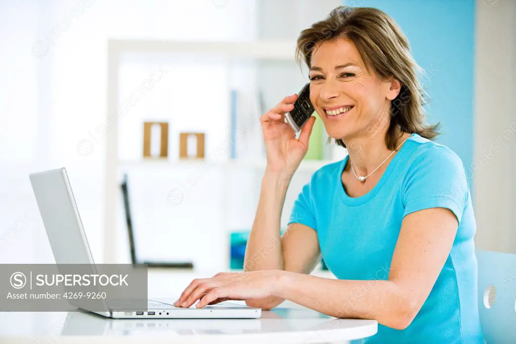 Woman using laptop computer and cell phone.