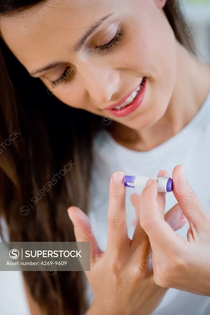 A diabetic person is checking her blood sugar level (self glycemia). A drop of blood obtained with a pen-like lancing device (here a single-use lancet) is placed on a test stick and analysed with blood glucose tester (glucometer).