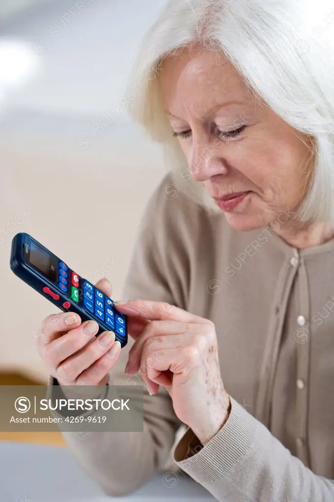 Senior woman using ergonomic cellphone, designed for elderly users with a larger keypad.