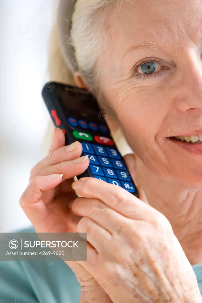 Senior woman using ergonomic cellphone, designed for elderly users with a larger keypad.