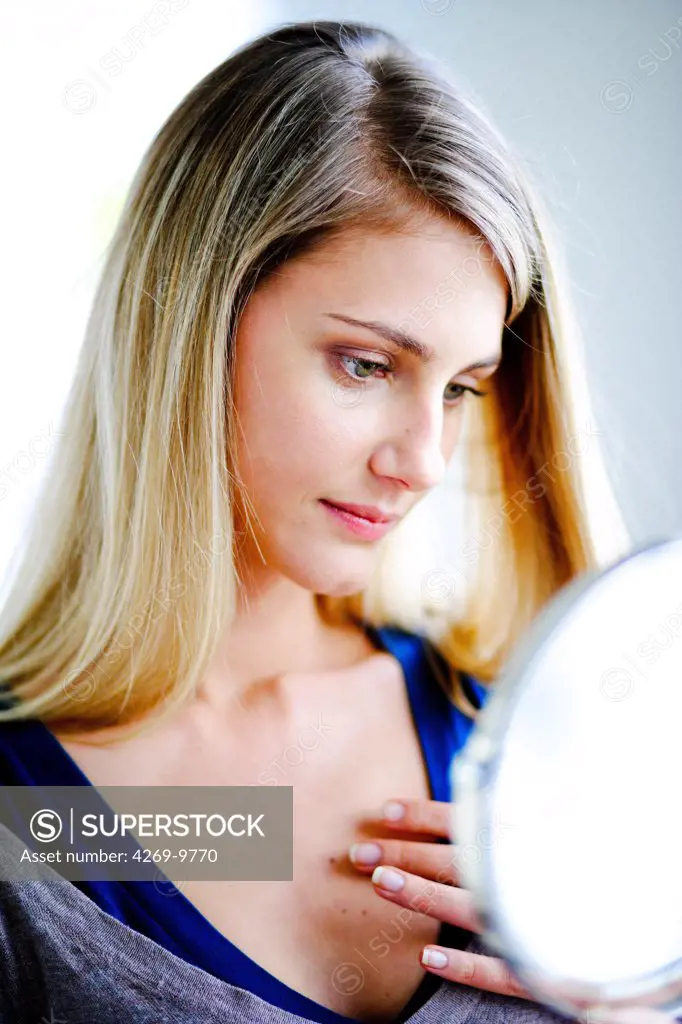 Woman inspecting a beauty mark in a mirror.