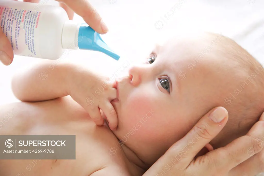 5 months old baby having his nose cleared with physiological saline solution spray.