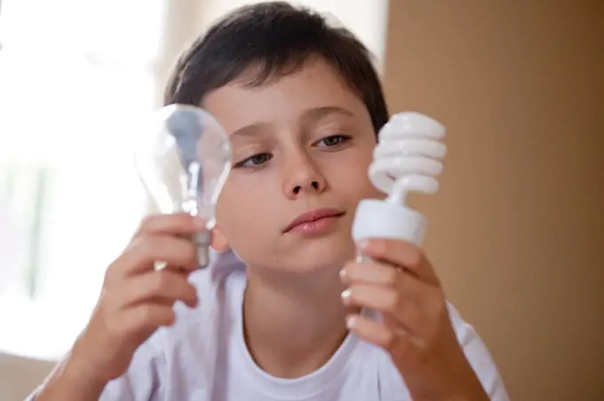 Boy holding energy saving lightbulb (right) and incandescent lightbulb (left).