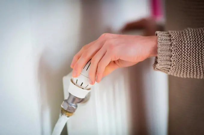Woman adjusting a thermostatic radiator valve on a domestic radiator
