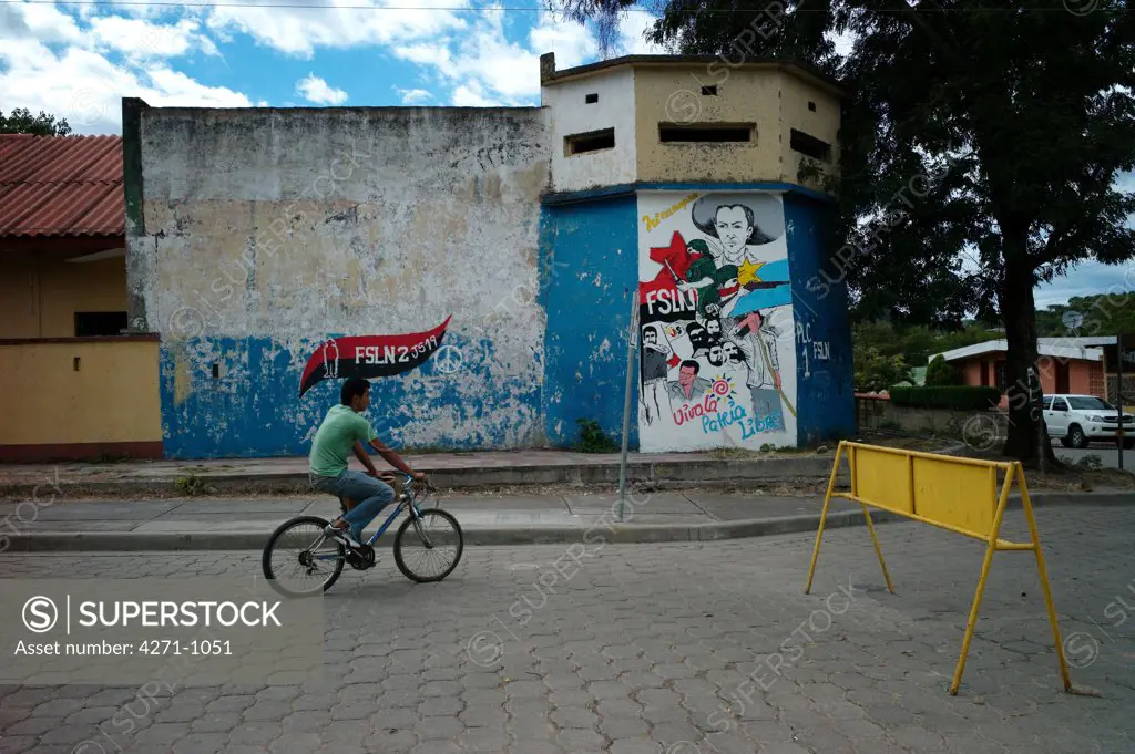 Nicaragua, Dipilto, Cyclist passing FSLN wall graffiti in Nueva Segovia department