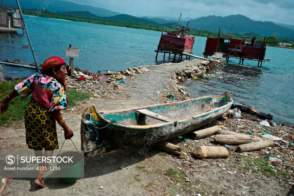 Panama, Kuna Yala, Elder woman carries bucket to outdoor latrine at coastal Indigenous guna village of Ustupu