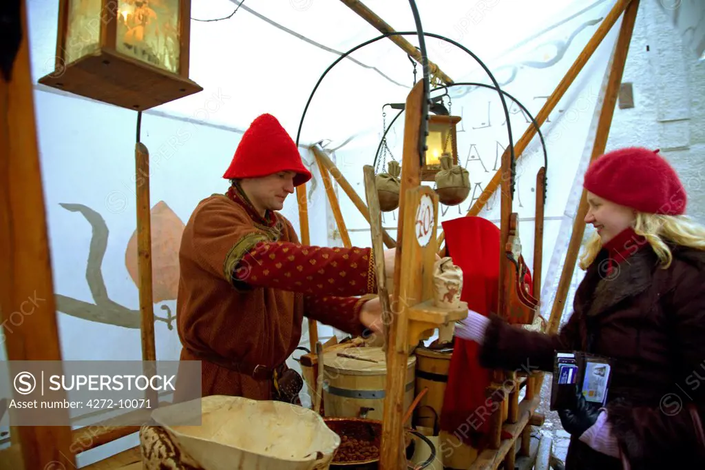 Estonia, Tallin; A street stand and seller in traditional clothes selling sweet warm almonds