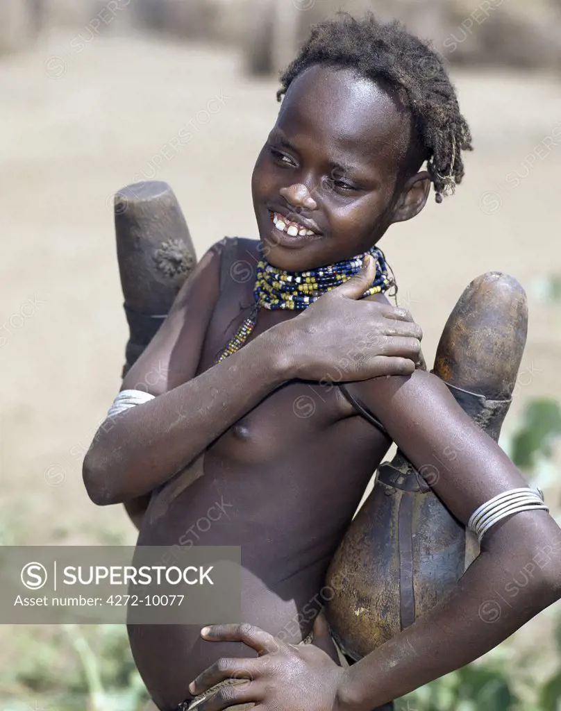 A young Dassanech girl carrying wooden milk containers.  Milk containers are regularly sterilized with smoke from aromatic wood or dry herbs.The Dassanech people live in the Omo Delta of southwest Ethiopia, one of the largest inland deltas in the world.