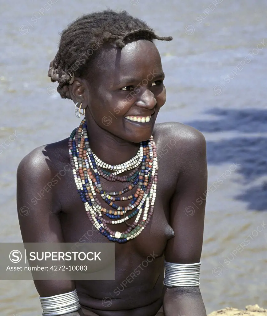A young Daasanech girl beside the Omo River.  Her hairstyle, necklaces and metal armbands are typical of her tribe.The Dassanech people live in the Omo Delta of southwest Ethiopia, one of the largest inland deltas in the world.