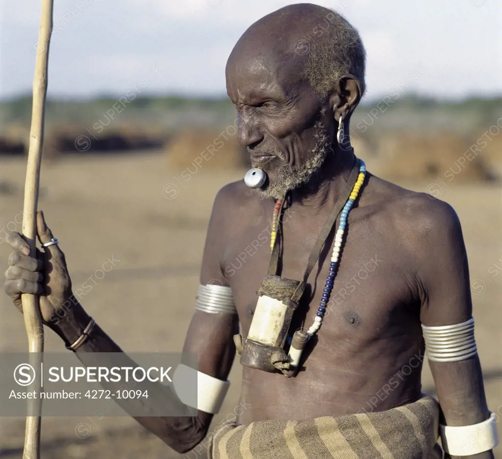 An old Dassanech man wearing a traditional metal lip ornament and metal earrings.  His broad ivory armbands and his ivory tobacco container hanging round his neck, are uncommon because elephants no longer frequent the Omo Delta.The Dassanech people live in the Omo Delta of southwest Ethiopia.