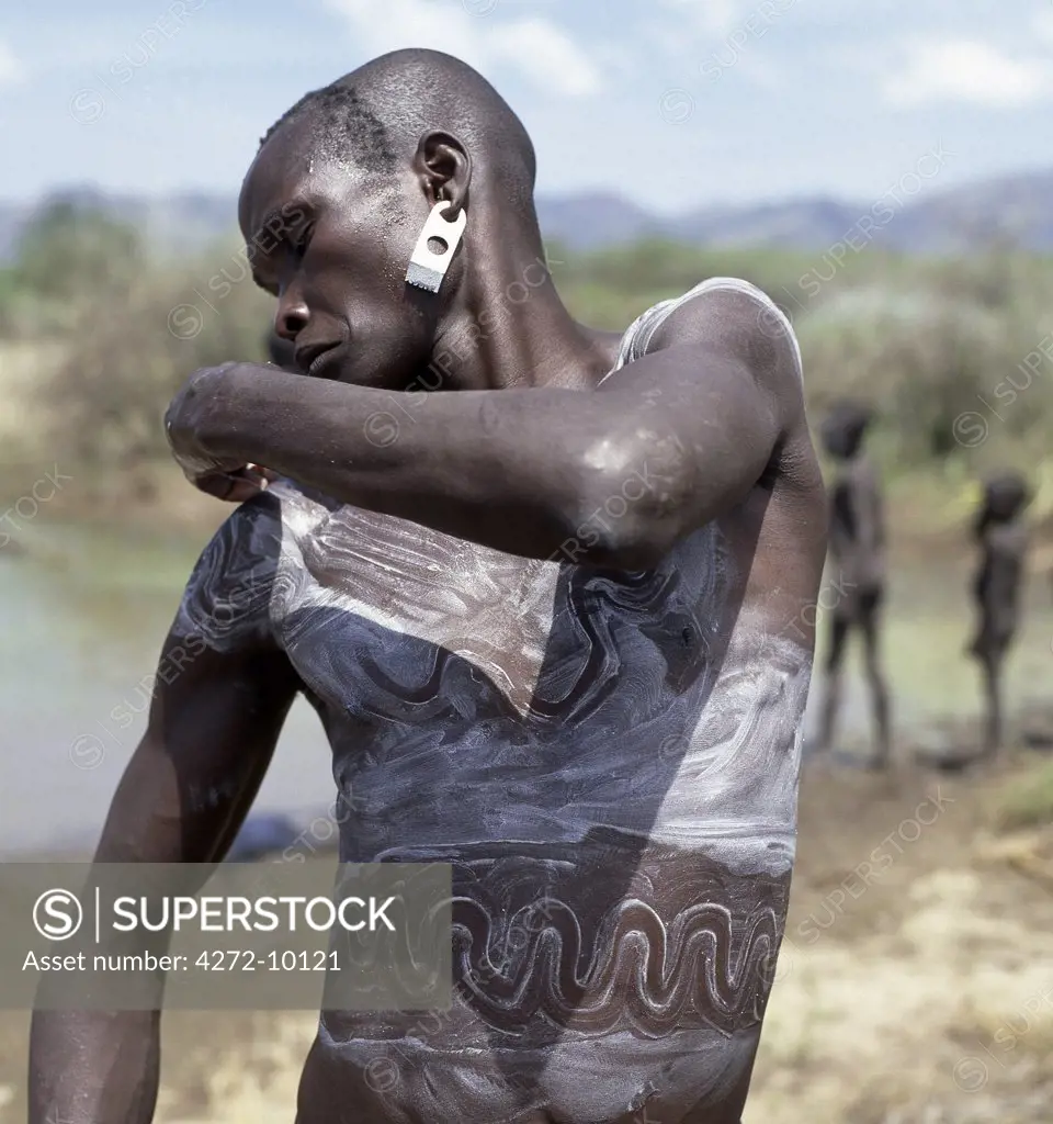 A Mursi man smears his body with a mixture of local chalk and water and then draws designs with his fingertips to enhance his physical appearance.The Mursi speak a Nilotic language and have affinities with the Shilluk and Anuak of eastern Sudan.  They live in a remote area of southwest Ethiopia along the Omo River.