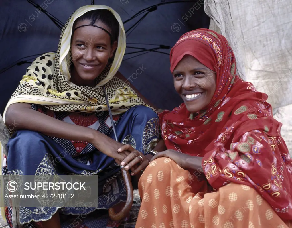 Two young women in colourful dresses and headscarves relax at Senbete market, which is an important weekly market close to the western scarp of the Abyssinian Rift. Afar nomads from the low lying arid regions of Eastern Ethiopia trek long distances there to barter with Amhara and Oromo farmers living in the fertile highlands.