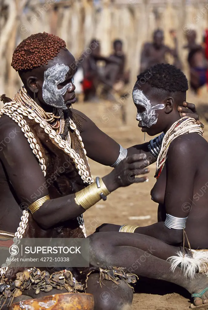 A Karo woman paints her daughters face with white chalk.  The mother has styled her hair with mud and ochre.  She wears a calfskin cape edged with cowrie shells, and layers of beads, bracelets and amulets.  A small Omotic tribe related to the Hamar, who live along the banks of the Omo River in southwestern Ethiopia.