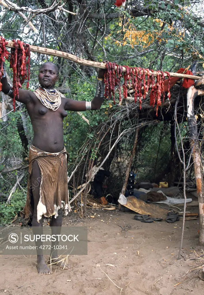 A Karo woman hangs meat from a slaughtered goat to dry on a pole outside her temporary camp on the bank of the Karo River.  A small Omotic tribe related to the Hamar, who live along the banks of the Omo River in southwestern Ethiopia, the Karo are renowned for their elaborate body painting using white chalk, crushed rock and other natural pigments.