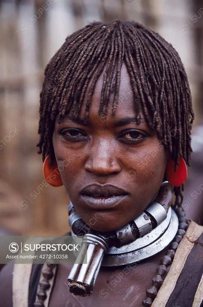 A Hamar woman in the village square of Dimeka.  Married women wear two heavy steel necklaces.  This woman wears an extra necklace with steel a steel phallic symbol which identifies her as a first wife.  She wears her hair long in a braided fringe matted with animal fat and ochre.