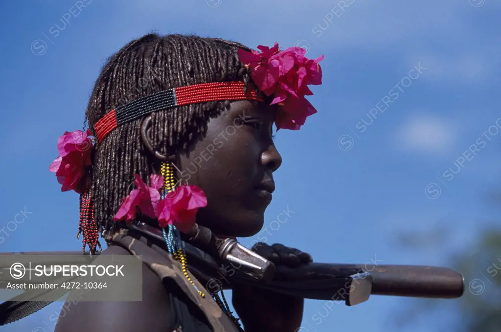 A Hamar woman wears the two heavy iron necklaces of a married woman and the extra necklace with phallic symbol that identifies her as a first wife.  Her hair is braided and reddened with a mixture of ochre and animal fat and decorated with bougainvillia flowers.