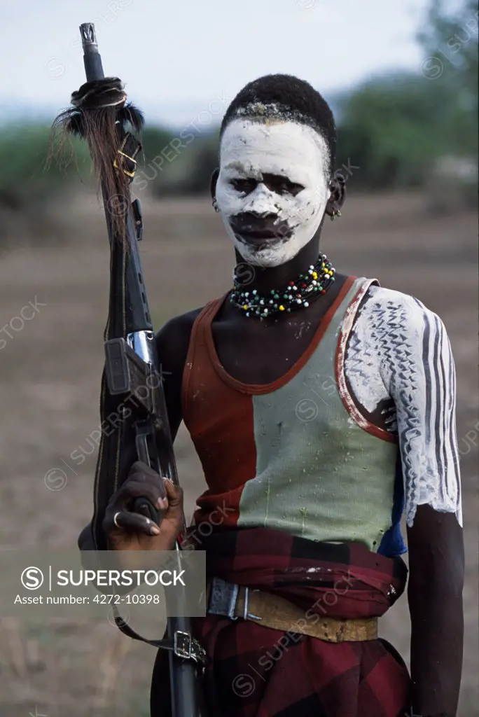 A Nyangatom warrior has painted his body and face in  preparation for a dance.  Most adult males carry rifles both as status symbols and in case of cattle raids or disputes with neighbouring tribes.  The Nyangatom or Bume are a Nilotic tribe of semi-nomadic pastoralists who live along the banks of the Omo River in south-western Ethiopia.