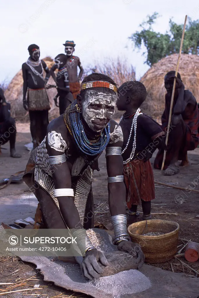 A Nyangatom woman grinds sorghum using two stones.  Typical of her tribe, she wears a heavily beaded calfskin skirt, multiple layers of bead necklaces and metal bracelets and amulets.  The Nyangatom or Bume are a Nilotic tribe of semi-nomadic pastoralists who live along the banks of the Omo River in south-western Ethiopia.