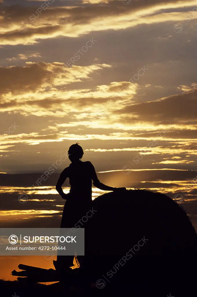 A Dassanech girl leaning against a bale of cattle fodder on a raised platform  is silhouetted against the evening sky at a settlement alongside the Omo River. Much the largest of the tribes in the Omo Valley numbering around 50,000, the Dassanech (also known as the Galeb, Changila or Merille) are Nilotic pastoralists and agriculturalists.