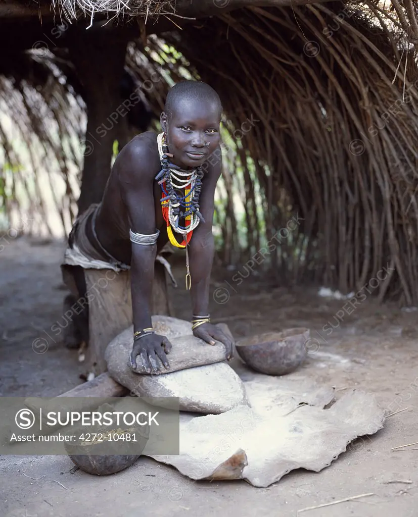 A Kwego woman grinds sorghum flour at the entrance to her hut.  The Kwego are a Nilotic tribe of semi-nomadic pastoralists who live along the banks of the Omo River in south-western Ethiopia.