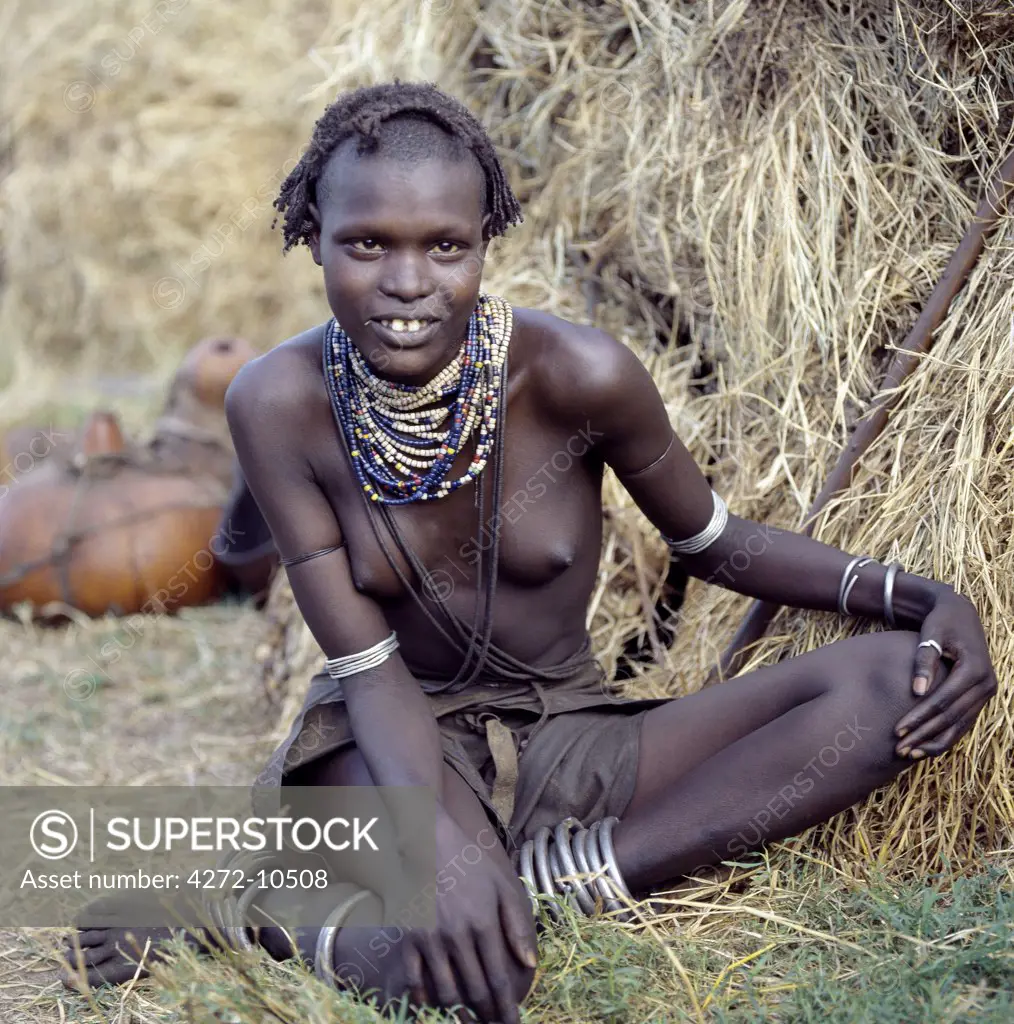 An attractive Dassanech girl sits outside her home in the Omo Delta. In the background are her gourds used for water and milk. Her leather skirt and adornment are typical of the girls of her tribe. Since the Omo Delta is one of the least accessible and least developed parts of East Africa the culture, social organization, customs and values of the people have changed less than elsewhere.
