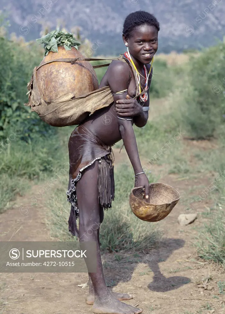 A girl of the Tsemay tribe of remote Southwest Ethiopia wears an attractively decorated leather skirt and apron.  She is returning home with water in the large gourd carried on her back. ,The Tsemay are a small tribe neighbouring the more numerous Hamar people with whom they share a common language.