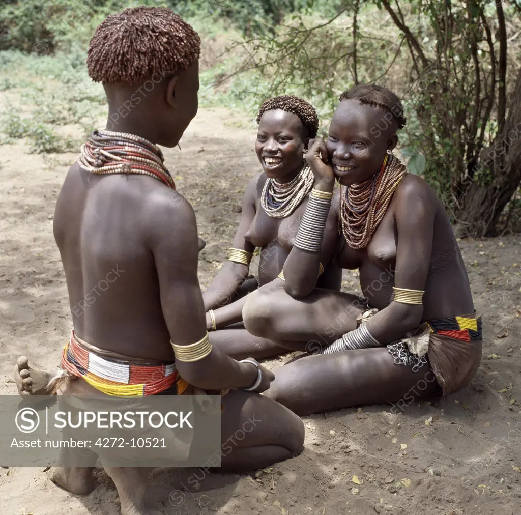 Karo girls chat in the shade of the riverine forest that lines the banks of the Omo River.  It is a tradition for girls to pierce a hole below the lower lip in which they place a thin piece of metal or a nail for decoration. The Karo are a small tribe living in three main villages along the lower reaches of the Omo River in southwest Ethiopia.